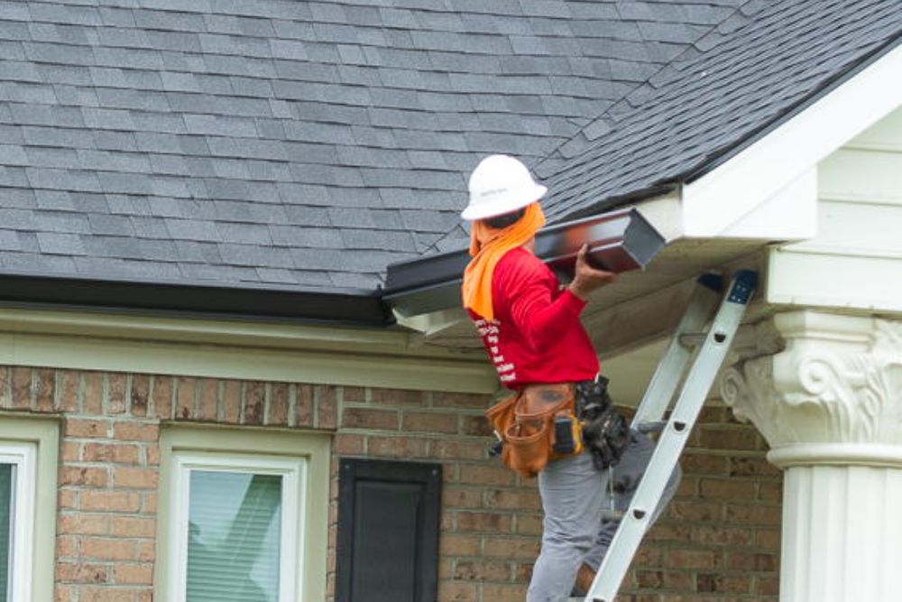 A man on a ladder performing roofing work on a house, showcasing our gutter roofing service in Spokane, WA.