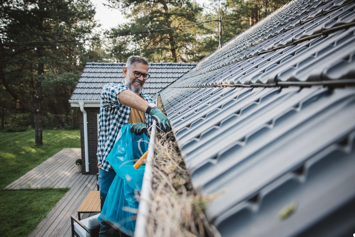 A man using a broom to clean the roof of his house on a sunny day.